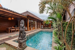 Une piscine ornée d’une statue, un patio abrité et une végétation luxuriante.