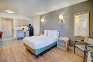 Hotellihuone, jossa on sänky, yöpöydät, tuoli, työpöytä, pieni keittiö ja peili.
