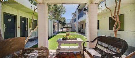 A covered outdoor area with wicker furniture, a table with flowers, and a view of the building's interior.