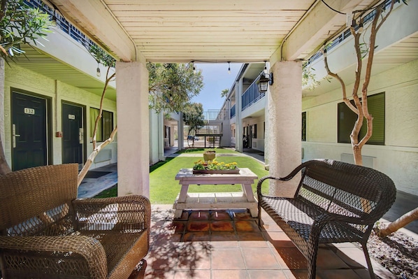 A covered outdoor area with wicker furniture, a table with flowers, and a view of the building's interior. - Tucson Studio Getaway | Augie Acuna Los Ninos Park — 1 mile (Tucson)