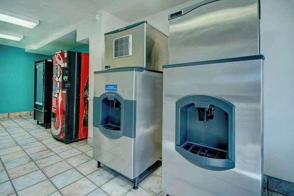 Een rij roestvrijstalen koelkasten met waterdispensers, een automaat en een deur met een bordje.