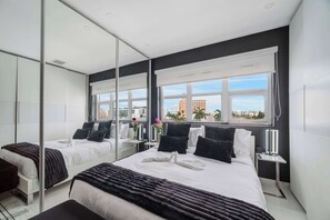 Una camera d'albergo moderna con un letto grande, un comodino, uno specchio e una finestra con vista sulla città.