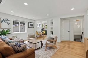 A modern living room with a sofa, armchair, coffee table, and a dining area with chairs. - Stylish 3BR Retreat w Pool Table & More (Seattle)