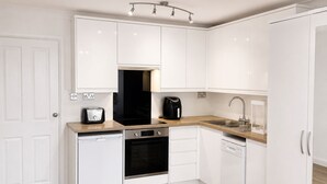 A modern kitchen with white cabinetry, a dishwasher, an oven, a coffee maker, and a sink. - Studio - Sleeps 2 - Wifi - Parking (Dunstable)