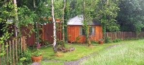 A wooden cabin with a sloped roof, surrounded by a wooden fence and lush greenery. - Unique Retreat Sleeps 2 with Hot Tub & Pets Ok (Bantry)