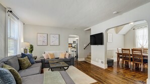 En moderne stue med en hjørnesofa, et sofabord og et spiseområde med træstole og et bord.