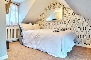 A bedroom with a bed, a window with curtains, a radiator, and a geometric-patterned wall. - House Sleeps 11 with Free Parking & WiFi (Birmingham)
