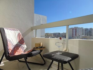 Ein Balkon mit einem Stuhl, einem kleinen Tisch, einem Glas Wasser und einem Strohhut.