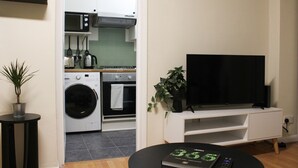 Una cucina moderna con microonde, forno e lavatrice, una TV a schermo piatto su un supporto bianco e un piccolo tavolo con un libro e un telecomando.