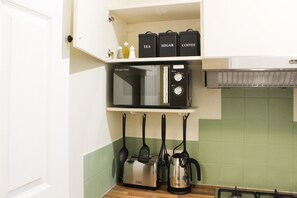 A kitchen with a microwave, toaster, kettle, and hanging utensils. - Cosy 1br Flat - 15mins to Central London (Croydon)