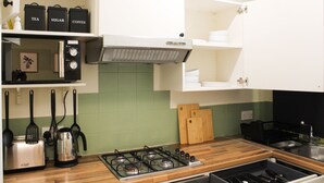 Cucina con piano cottura a gas, tostapane, bollitore ed scaffali con contenitori etichettati per tè, zucchero e caffè.