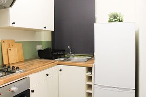 A compact kitchen with a wooden countertop, a built-in oven, a sink, and a white refrigerator. - Cosy 1br Flat - 15mins to Central London (Croydon)