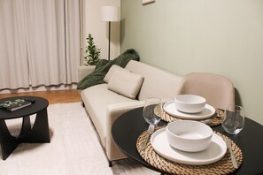 Ein Wohnzimmer mit einer Couch, einem Couchtisch, einem Esstisch mit Tellern und Gläsern sowie einer Lampe.