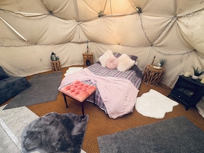 A cozy tent room with a bed, pillows, a bench, rugs, and small side tables. - Charming Retreat in Pewsey Countryside (Pewsey)