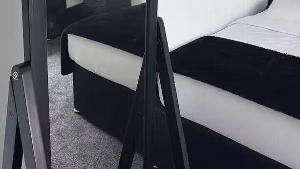 Quarto de hotel moderno com cama de moldura preta, painel de cabeceira branco, mesa de cabeceira com abajur e uma grande pintura abstrata na parede.