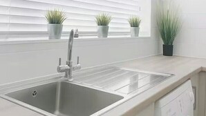 Uma cozinha moderna com uma pia dupla, máquina de lavar e plantas em vasos no parapeito da janela.