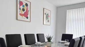 Uma área de refeições com uma mesa retangular, cadeiras pretas e quadros nas paredes.