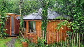 Eine Holzhütte mit Veranda, umgeben von einem Holzzaun und üppigem Grün.