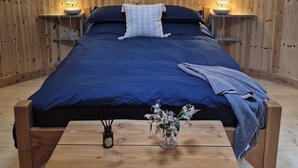 Ein Zeltraum mit einem Bett, Nachttischlampen, einem Holztisch und einer Vase mit Blumen.