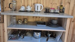 Ein Holzinterieur mit Regalen, auf denen Geschirr, eine Kaffeemaschine und ein gerahmtes Bild zu sehen sind.
