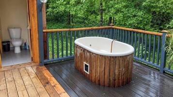 Une terrasse en bois avec un jacuzzi, une rambarde en bois et une vue sur une forêt verdoyante.