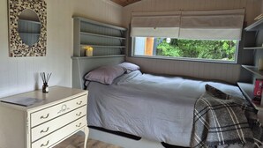 Une chambre à coucher comprenant un lit, un bureau avec des tiroirs, un miroir, des étagères et une fenêtre donnant sur un paysage verdoyant.