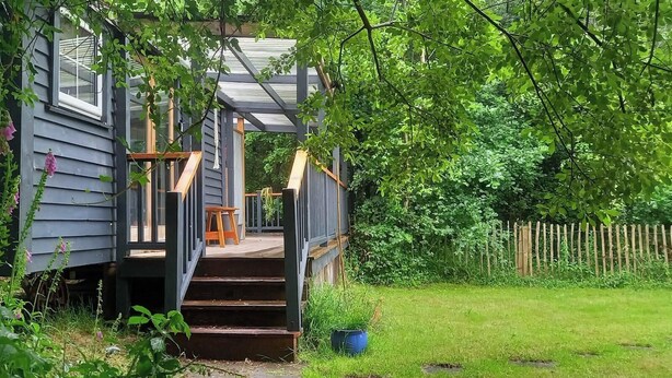 Une maison en bois avec un porche, des marches menant à une porte et une clôture en bois en arrière-plan.