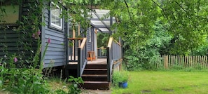 A wooden house with a porch, steps leading to a door, and a wooden fence in the background. - Sheperd's Hut, Sleeps 2 with Hot Tub and Garden (Bantry)