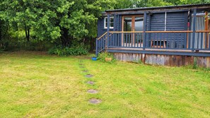 Une cabane en bois dotée d’une terrasse, entourée d’une cour verdoyante et d’une clôture en bambou.