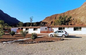 A row of white motel buildings with a car parked in front, set against a mountainous backdrop. - Country House Near Fataga & Maspalomas (San Bartolome de Tirajana)