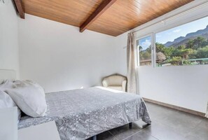 A bedroom with a bed, a chair, a window with a view of mountains, and a wooden ceiling. - Country House Near Fataga & Maspalomas (San Bartolome de Tirajana)