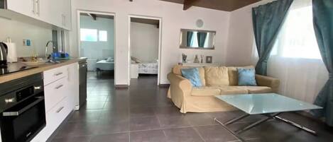 A modern living space with a kitchen, a sofa, a glass coffee table, and a dining area.