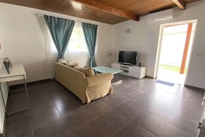 A living room with a sofa, a TV on a stand, a small table, and a door leading outside. - Finca House by Fataga Maspalomas (San Bartolome de Tirajana)