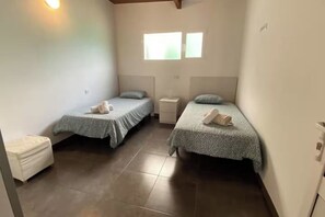 A small, clean room with two single beds, a white bench, and a window providing natural light. - Finca House by Fataga Maspalomas (San Bartolome de Tirajana)