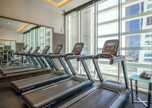 Une salle de sport équipée de plusieurs tapis de course, de grandes fenêtres et offrant une vue sur les bâtiments environnants.