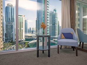 Habitación de hotel moderna con un gran ventanal que ofrece vistas a la ciudad, una mesa redonda con un florero y dos sillas.