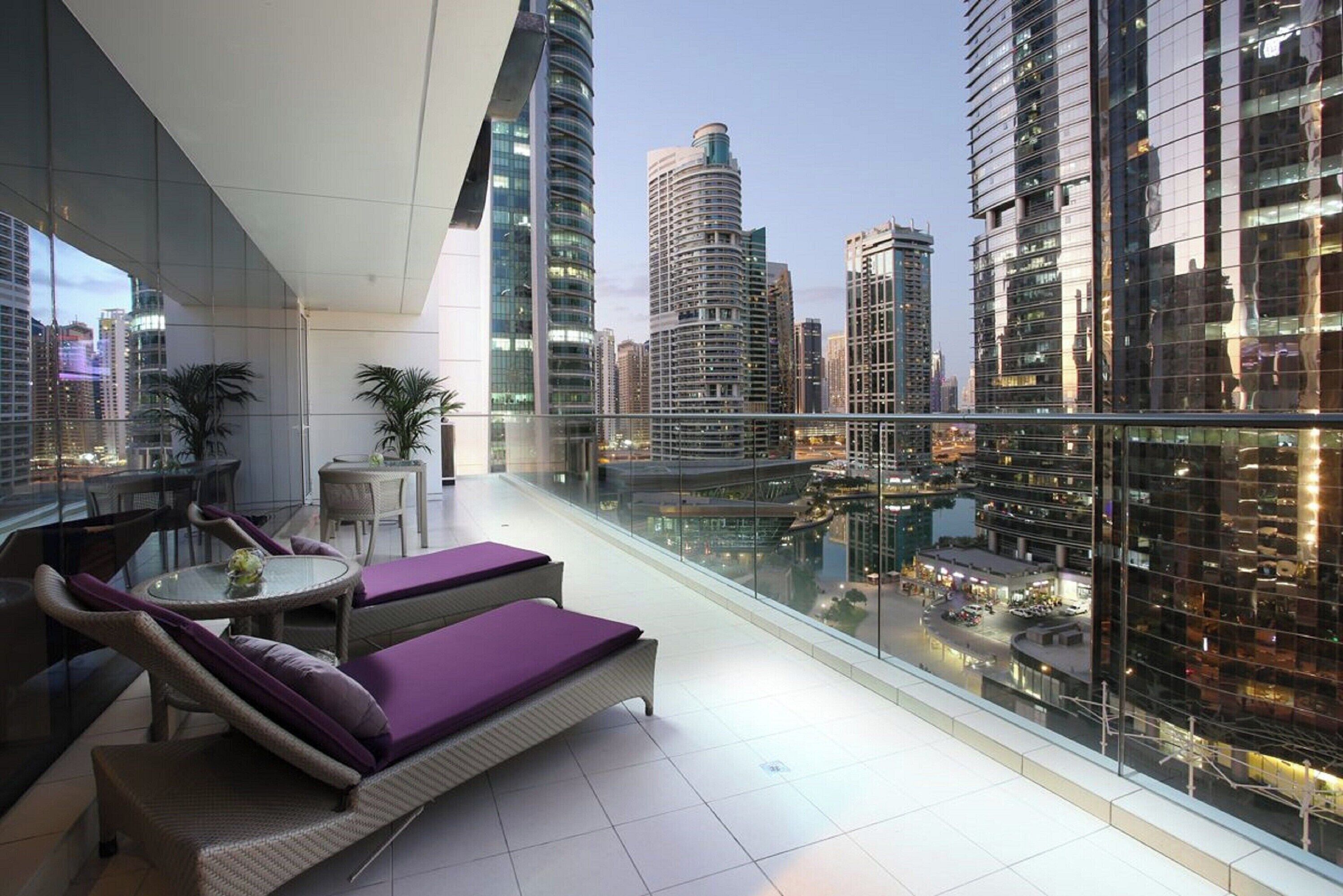 A modern balcony with wicker furniture, a glass table, and a city view.