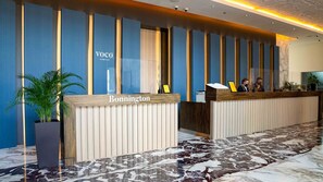 Un comptoir d’accueil d’hôtel avec une plaque nominative indiquant « Bonnington » et une enseigne au-dessus indiquant « Voco An Inho Hotel ».