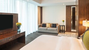A hotel room with a large bed, a TV, a sofa, a small table, and a mirror. - voco Bonnington | Corner Deluxe Suite | Pool, Sauna + Steam, Marina Minutes (Dubai)