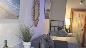 A bedroom with a bed, a bedside table with a lamp, a potted plant, and a door. - Beachfront Studio Suite Downhill Free Parking (Coleraine)
