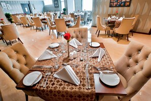 Un comedor con mesas dispuestas para cuatro, cada una con platos blancos, cubiertos y un centro de mesa.