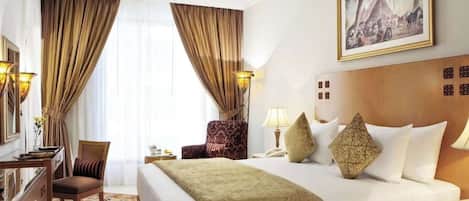 A hotel room with a large bed, a desk, a chair, a lamp, and a painting on the wall.