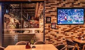 A restaurant interior with a brick wall, a mounted TV displaying a sports game, and a bar area with shelves and bottles.