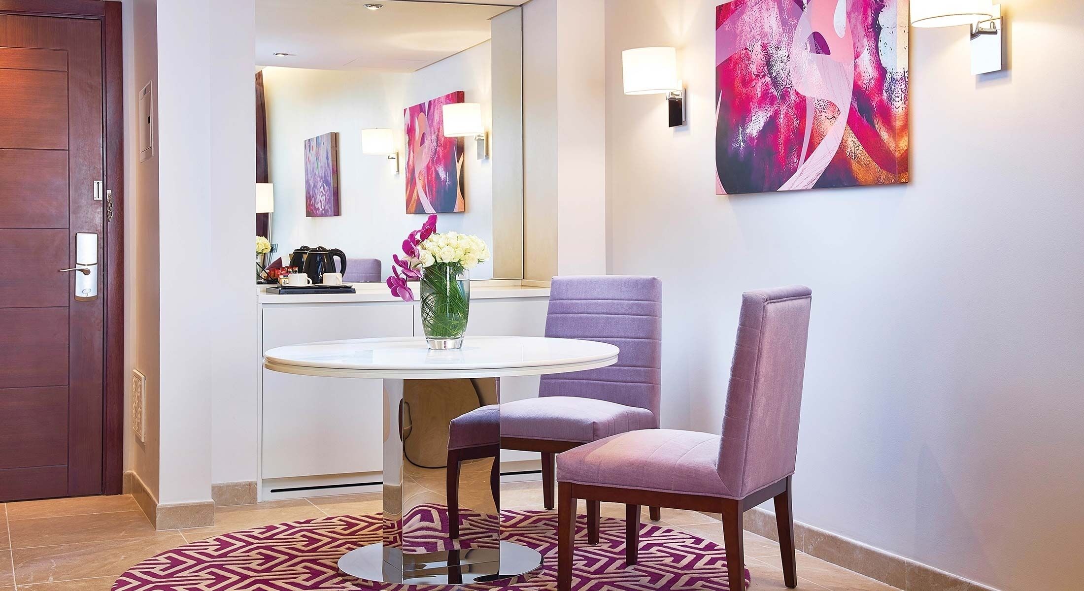 Eine Hotelhalle mit einem runden Tisch, violetten Stühlen, einer Blumenvase und abstrakter Kunst an den Wänden.