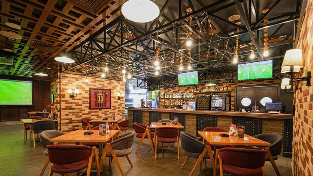 En restaurant med træborde og stole, et barområde og et skærm, der viser en sportsbegivenhed.