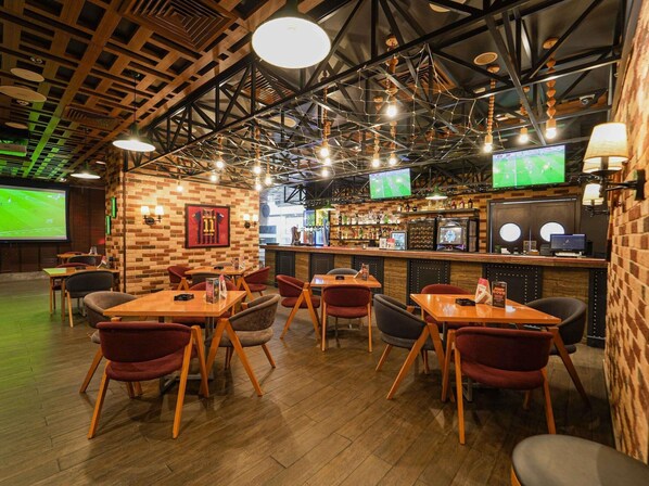 En restaurant med træborde og stole, et barområde og et skærm, der viser en sportsbegivenhed.