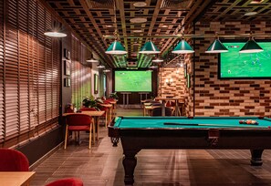 A billiards room with a pool table, red chairs, and a television displaying a sports game. - Mercure BH | 1BR City | Sheikh Zayed Rd Base Near Internet + Media City (Dubai)
