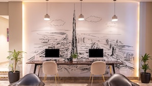 Sala de conferência com um grande mural na parede, dois monitores de computador, quatro cadeiras e dois vasos de plantas.