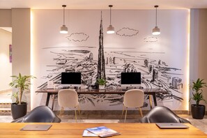 A conference room with a large wall mural, two computer monitors, four chairs, and two potted plants. - Mercure BH | 1BR City | Sheikh Zayed Rd Base Near Internet + Media City (Dubai)