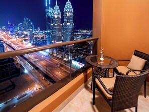 A balcony with a glass railing, a round table with two chairs, and a view of a cityscape at night. - Mercure BH | 1BR City | Sheikh Zayed Rd Base Near Internet + Media City (Dubai)